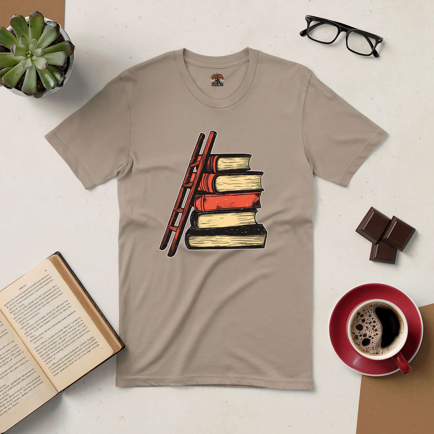 "Reaching New Heights Tee with book and ladder design, symbolizing the journey of readers exploring new stories on beige shirt."