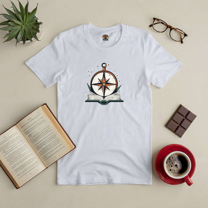 White tee with compass and open book design, surrounded by coffee, glasses, chocolate, and a potted plant, inspires self-discovery.