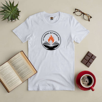 White "Lit Happens, But Books Heal" tee with open book and flame design, surrounded by a book, coffee, chocolate, glasses, and plant.