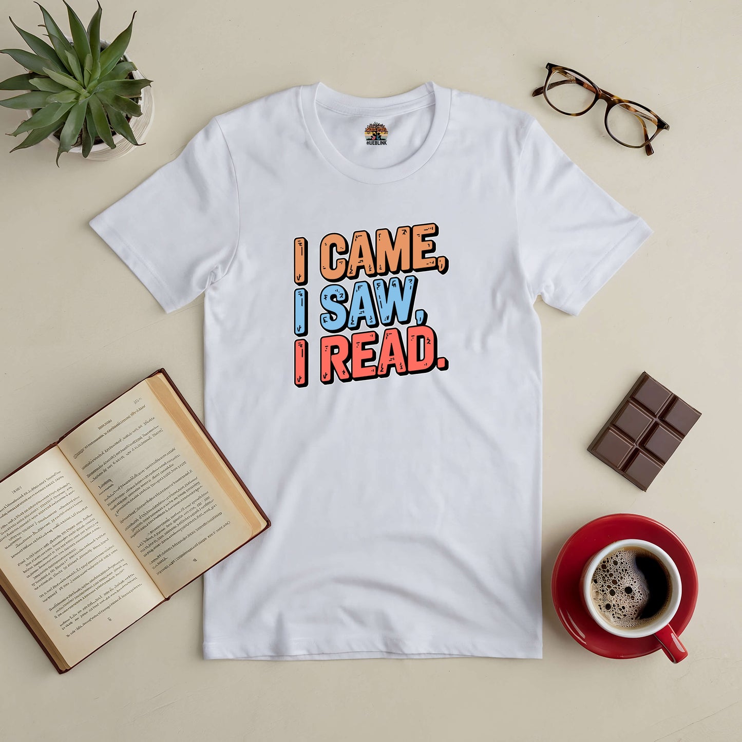 "I Came, I Saw, I Read tee on a table with coffee, chocolate, glasses, open book, and plant"