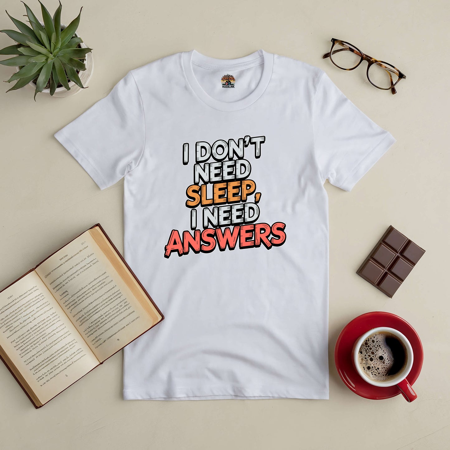 "I Don't Need Sleep, I Need Answers Tee with open book, glasses, and coffee on table"