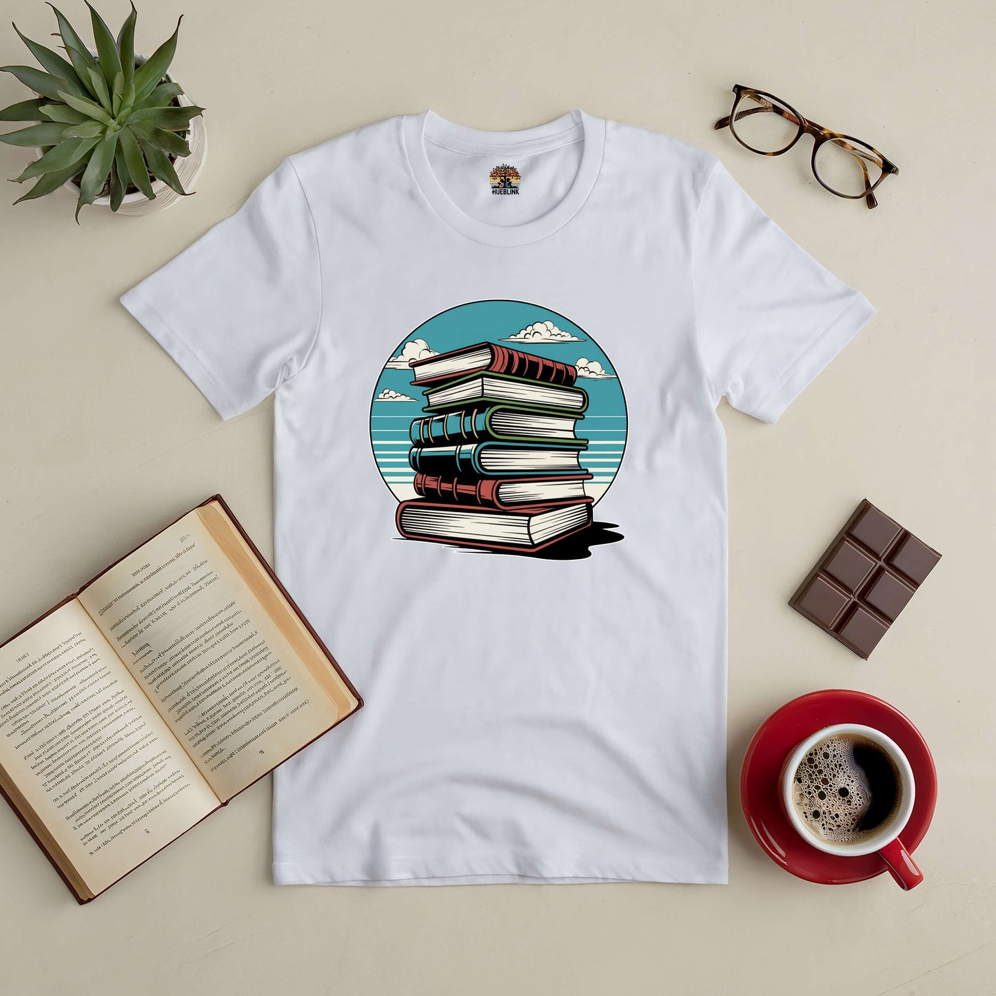 Silent Knowledge Tee with book stack design, serene sky graphic, for introspective readers. Displayed with coffee, glasses, and an open book.