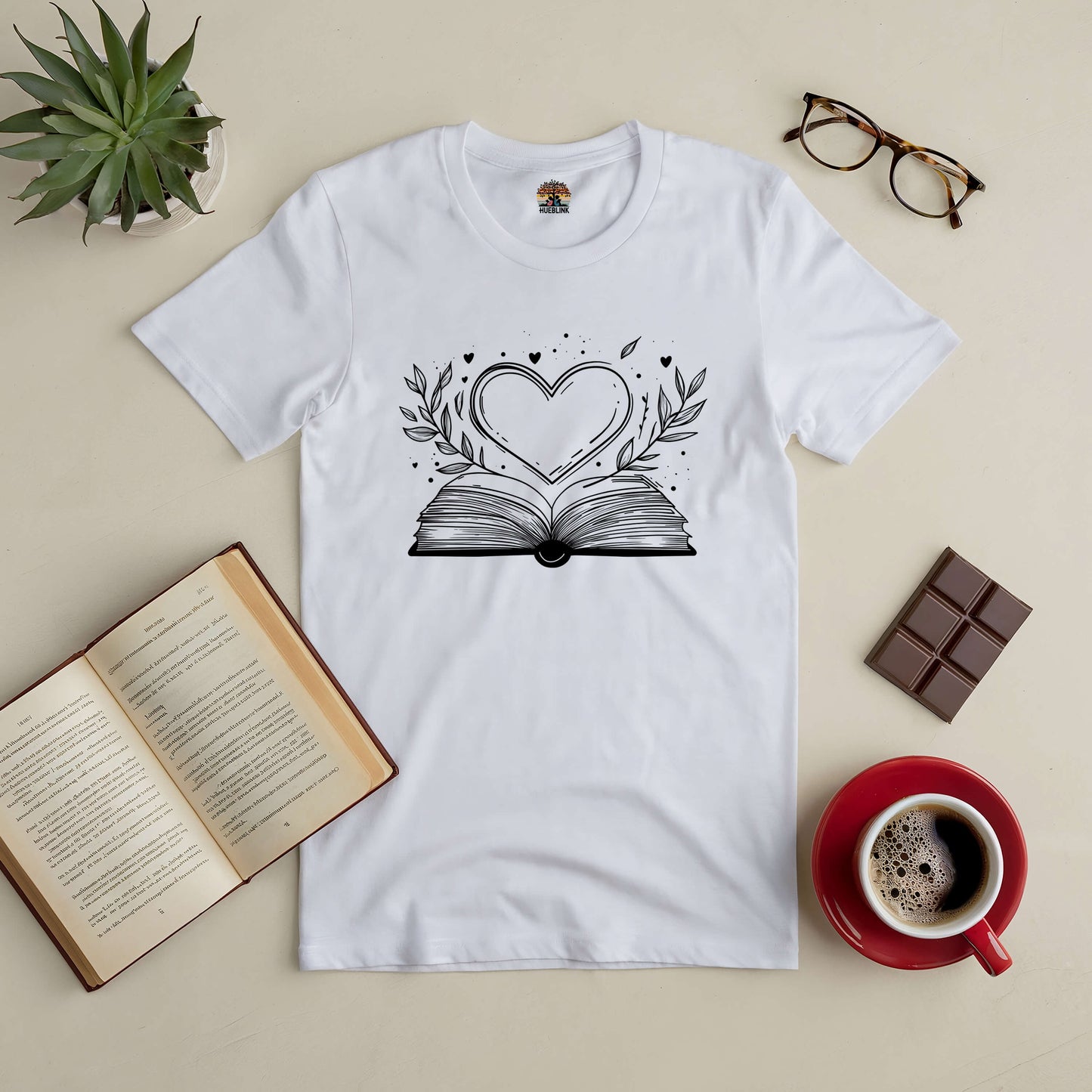 "Love Stories Tee with heart and book design, surrounded by coffee, glasses, and open book, ideal for romance enthusiasts."