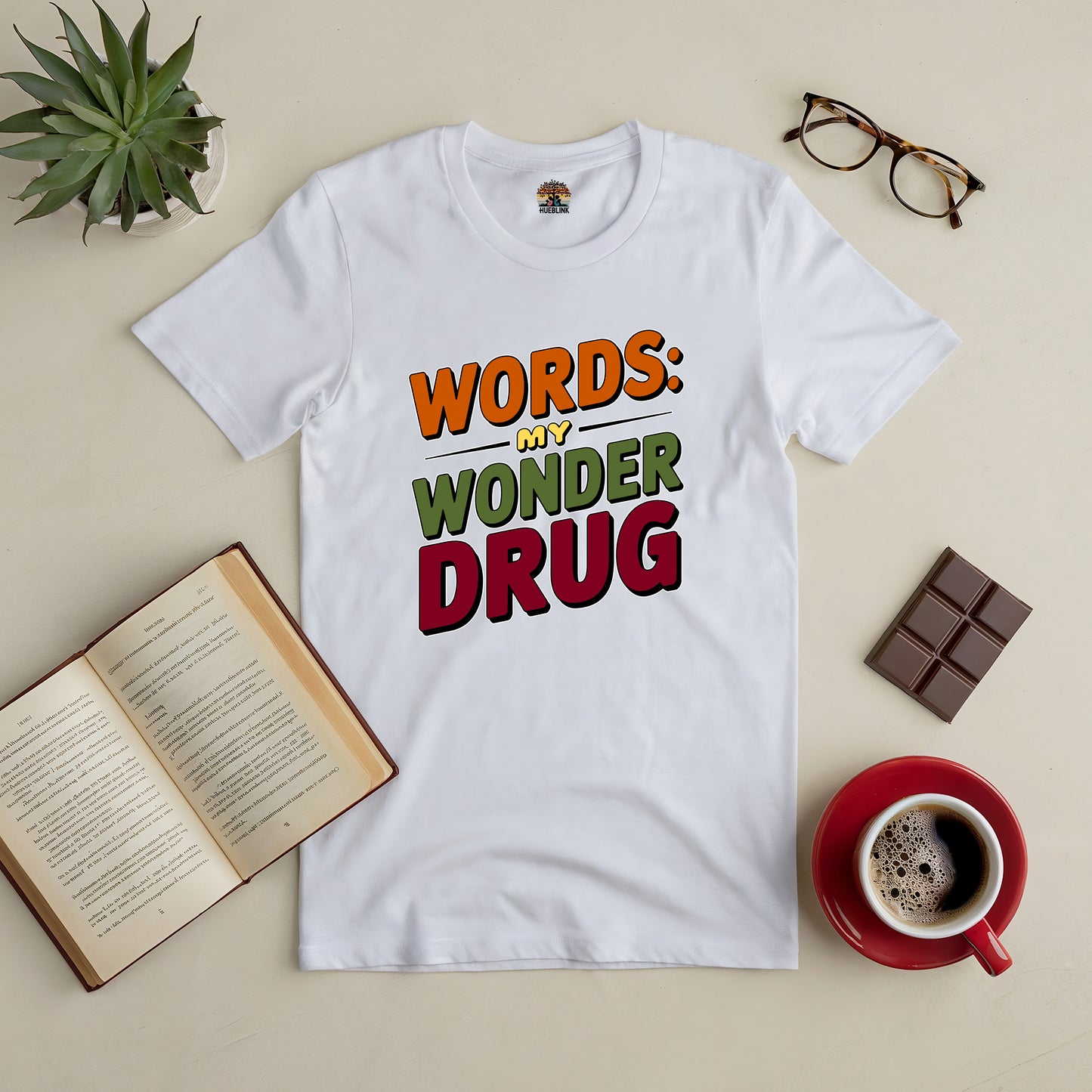 "Word Therapy Tee with 'Words: My Wonder Drug' design, surrounded by book, glasses, chocolate, and coffee on a table"