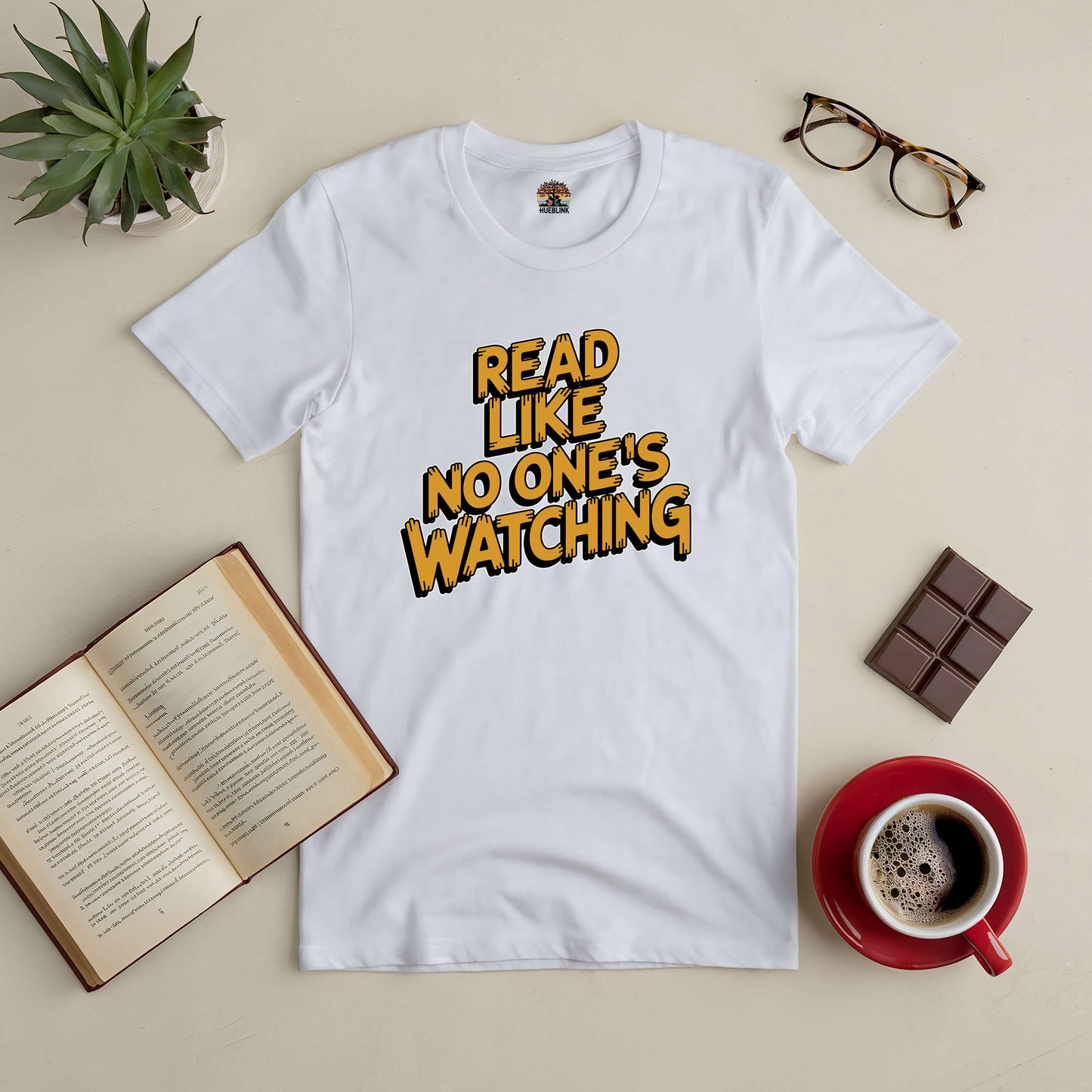 "Read Like No One's Watching tee with open book, coffee, glasses, and chocolate on a table"