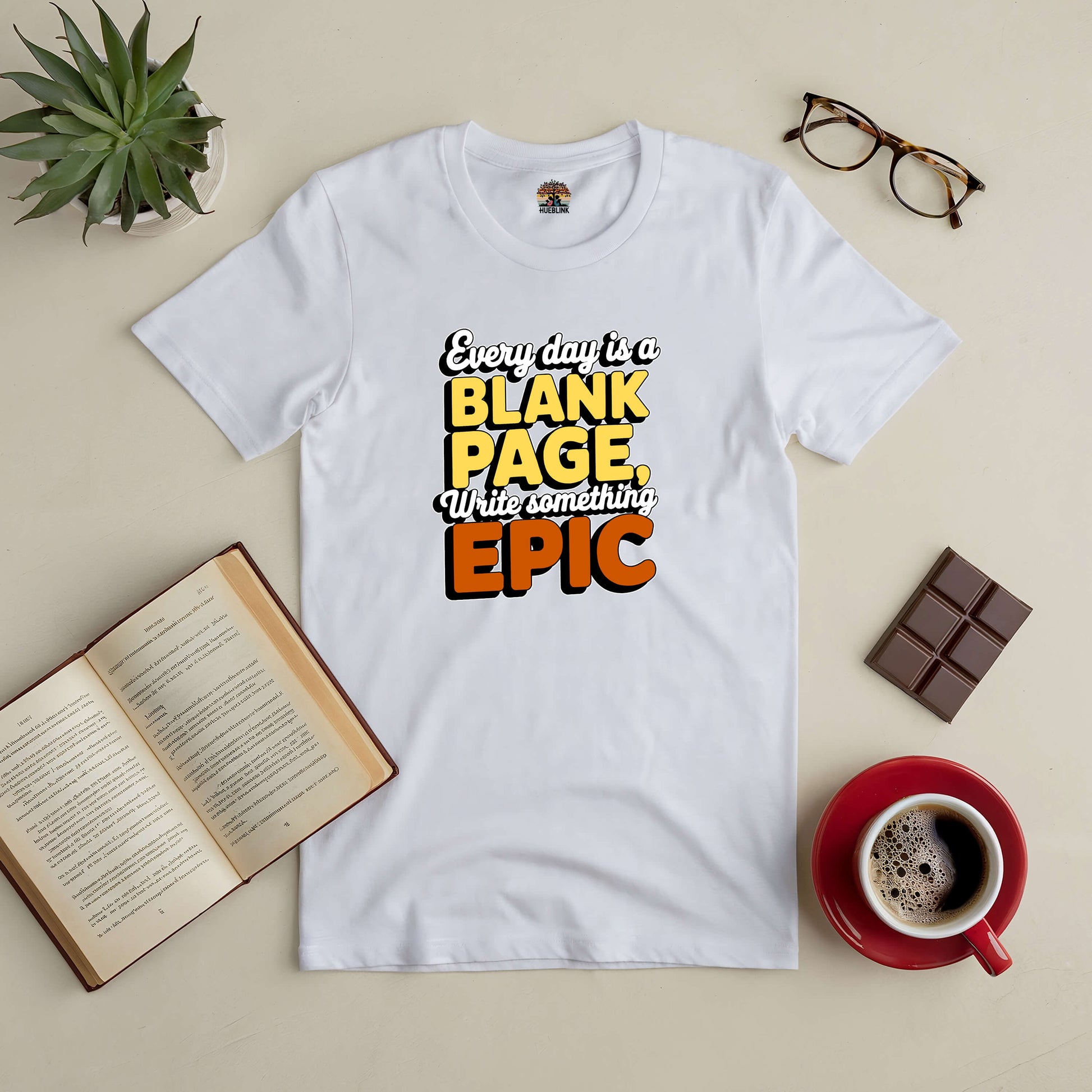 "Every Day is a Blank Page Tee, inspiring epic moments, surrounded by book, coffee, glasses, chocolate, and plant"