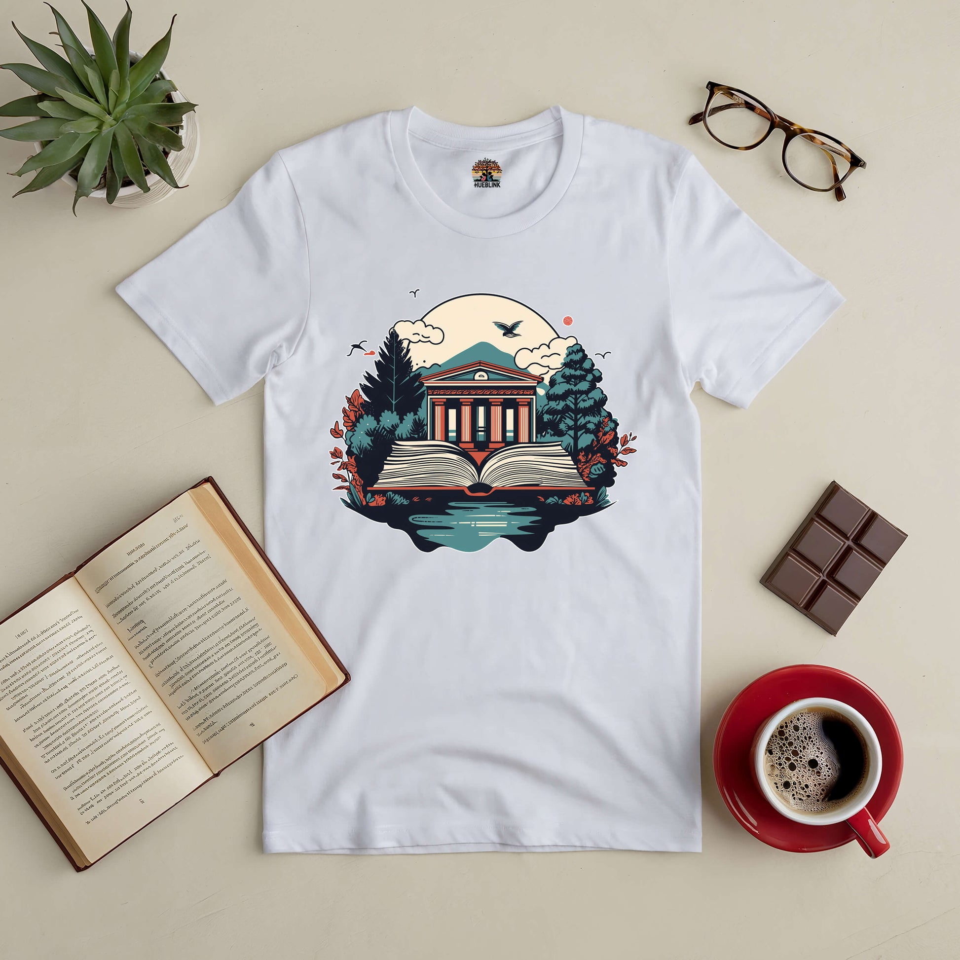 "Gateway to Knowledge Tee with nature and library design, surrounded by open book, coffee, and glasses for a wisdom-filled vibe."