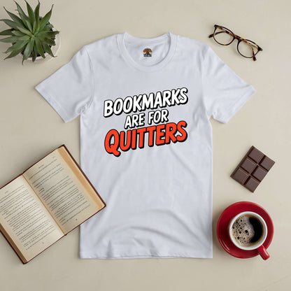 White tee with "Bookmarks Are for Quitters" text, surrounded by an open book, coffee, glasses, and a plant on a beige surface.